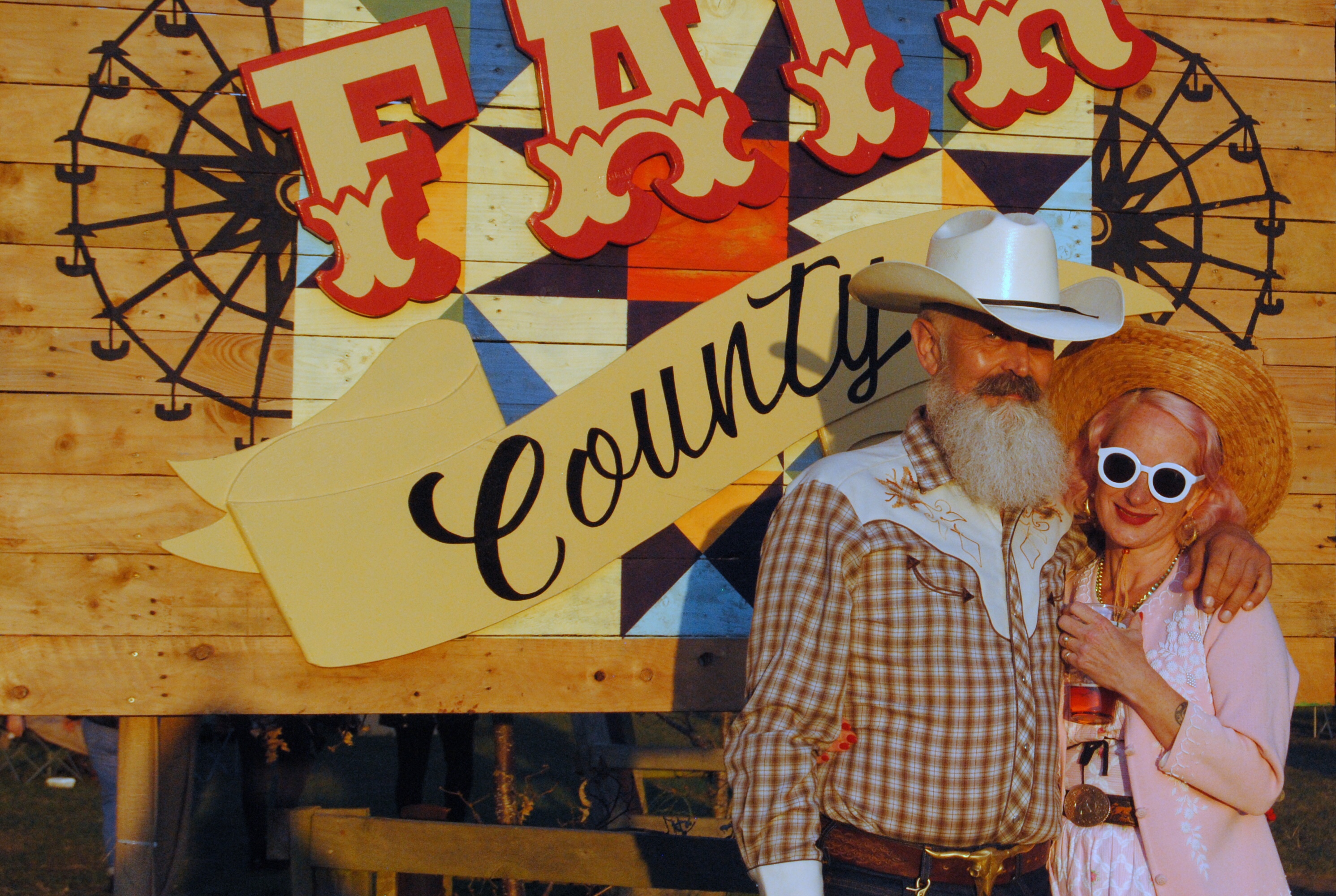Couple in western wear standing in front of county fair sign at Lond Road Festival