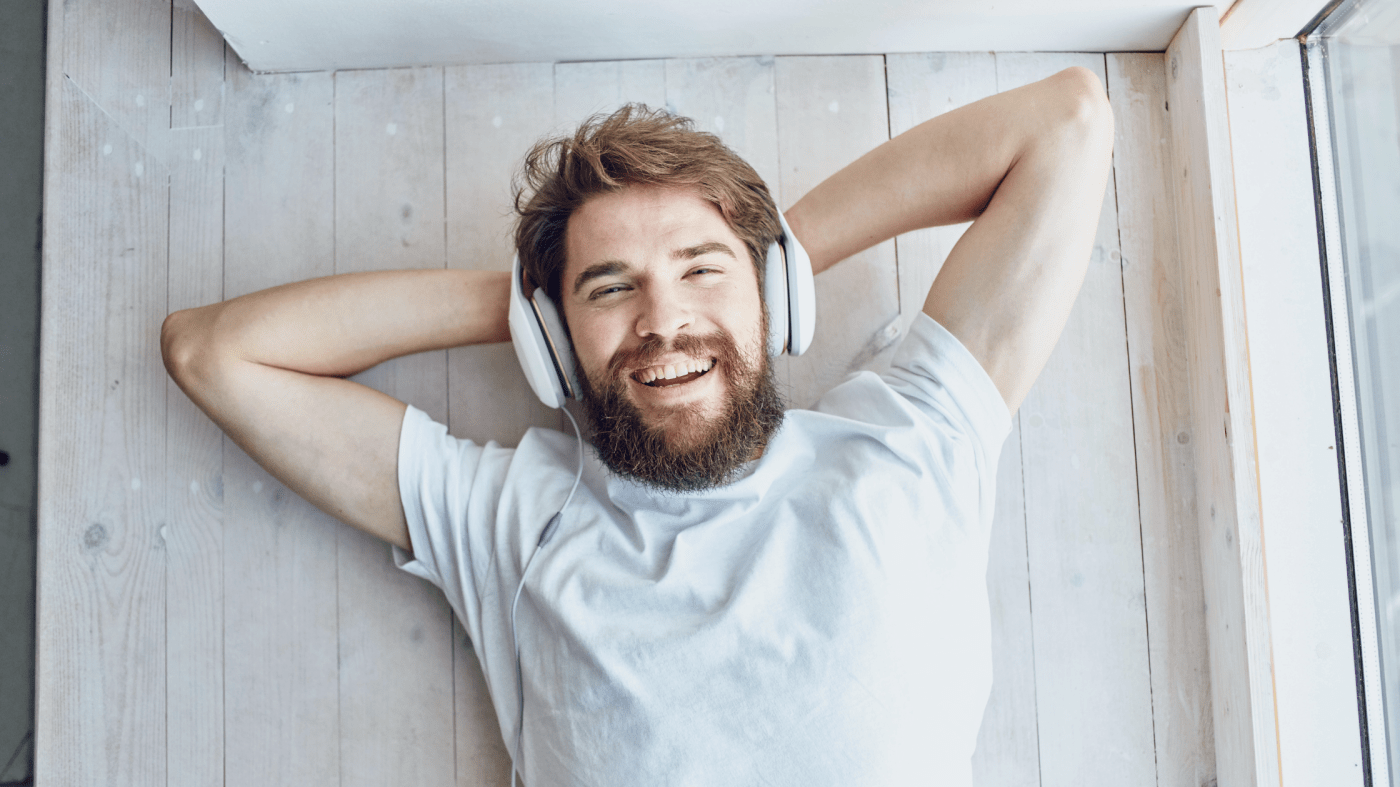 Man listening to music on headphones, lying on his back with hands beding his head and a big smile.