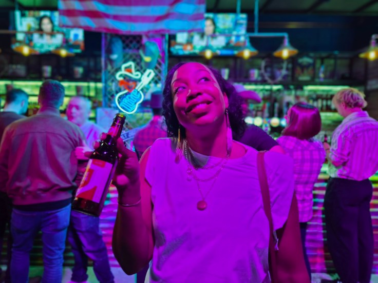 Woman stands in bar holding a beer