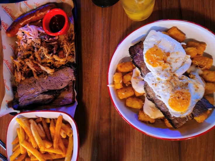 a tray of bbq meat, a bowl o fchips and a plate with bristket, fried eggs and tater tots.