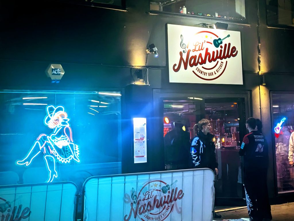 Exterior of Lil Nashville Bristol bar with neon cowgirl sign and security staff outside.